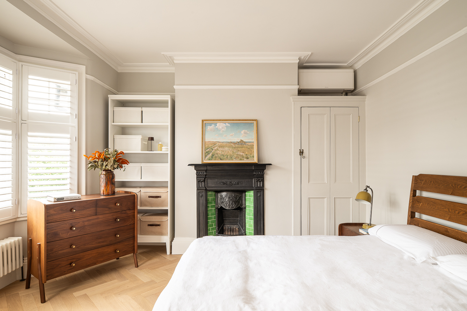Bedroom with bay window shutters, timber furniture, period fireplace, and built-in storage.
