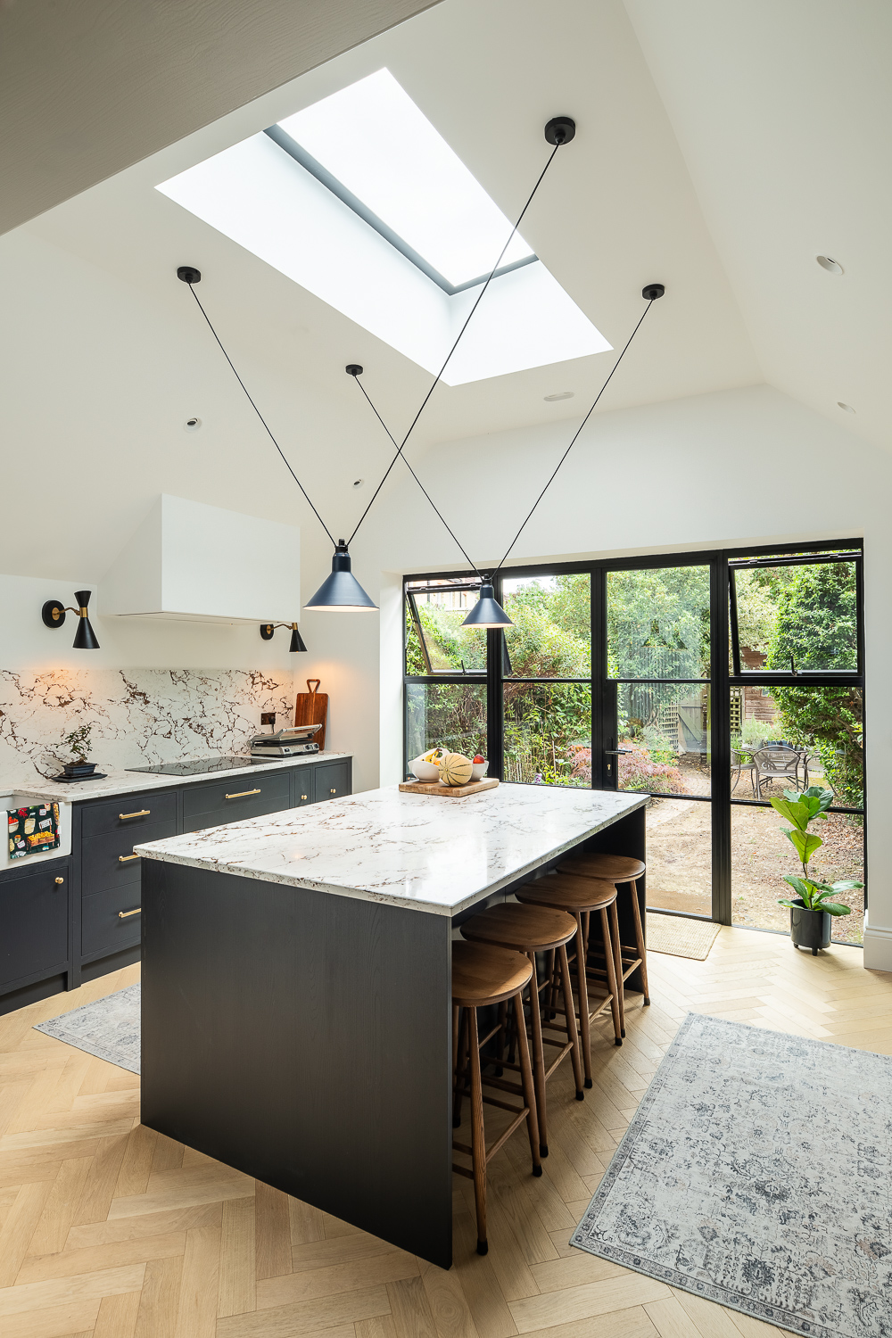 Kitchen extension with marble island, skylight, pendant lighting, and steel-framed garden doors.