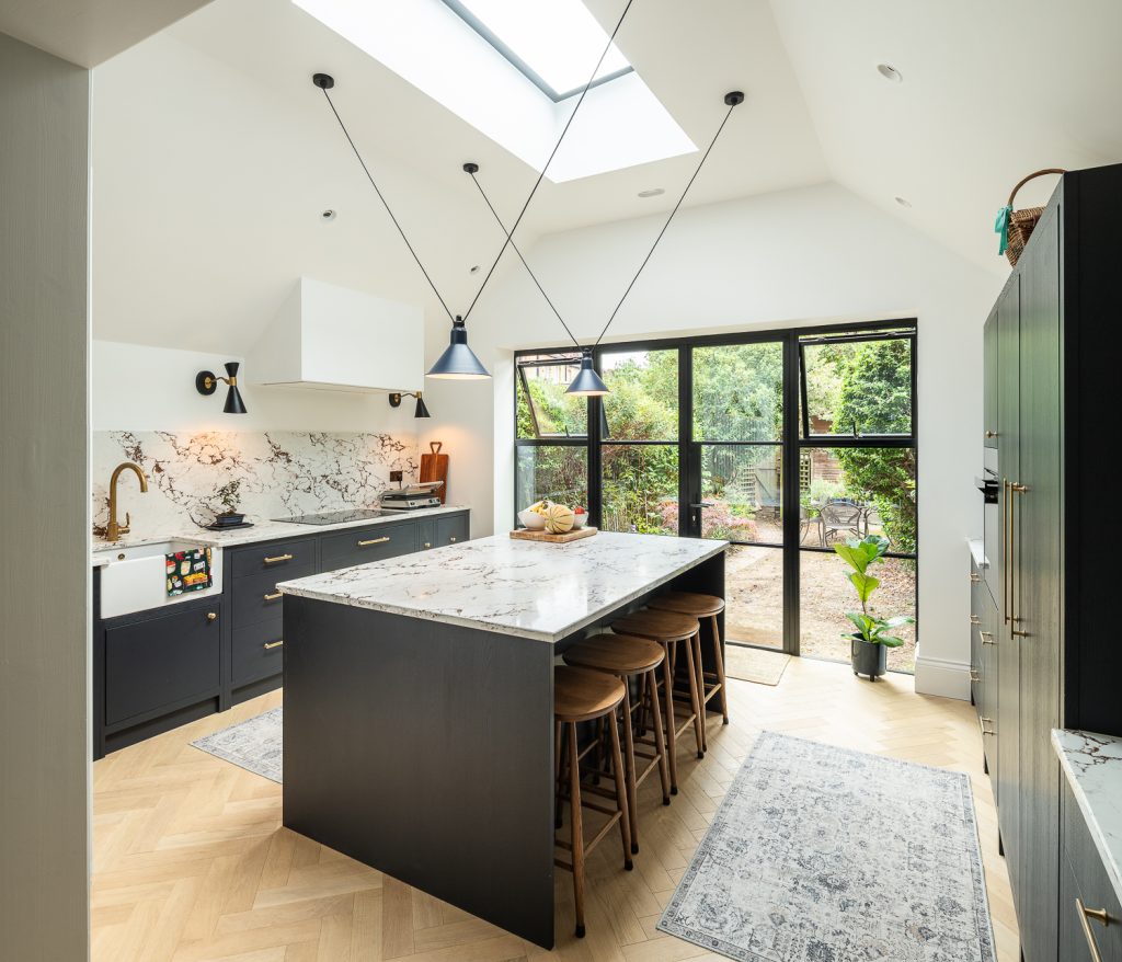 Kitchen extension interior with skylight, marble island, dark cabinetry, and steel-framed garden doors in an Edwardian home.