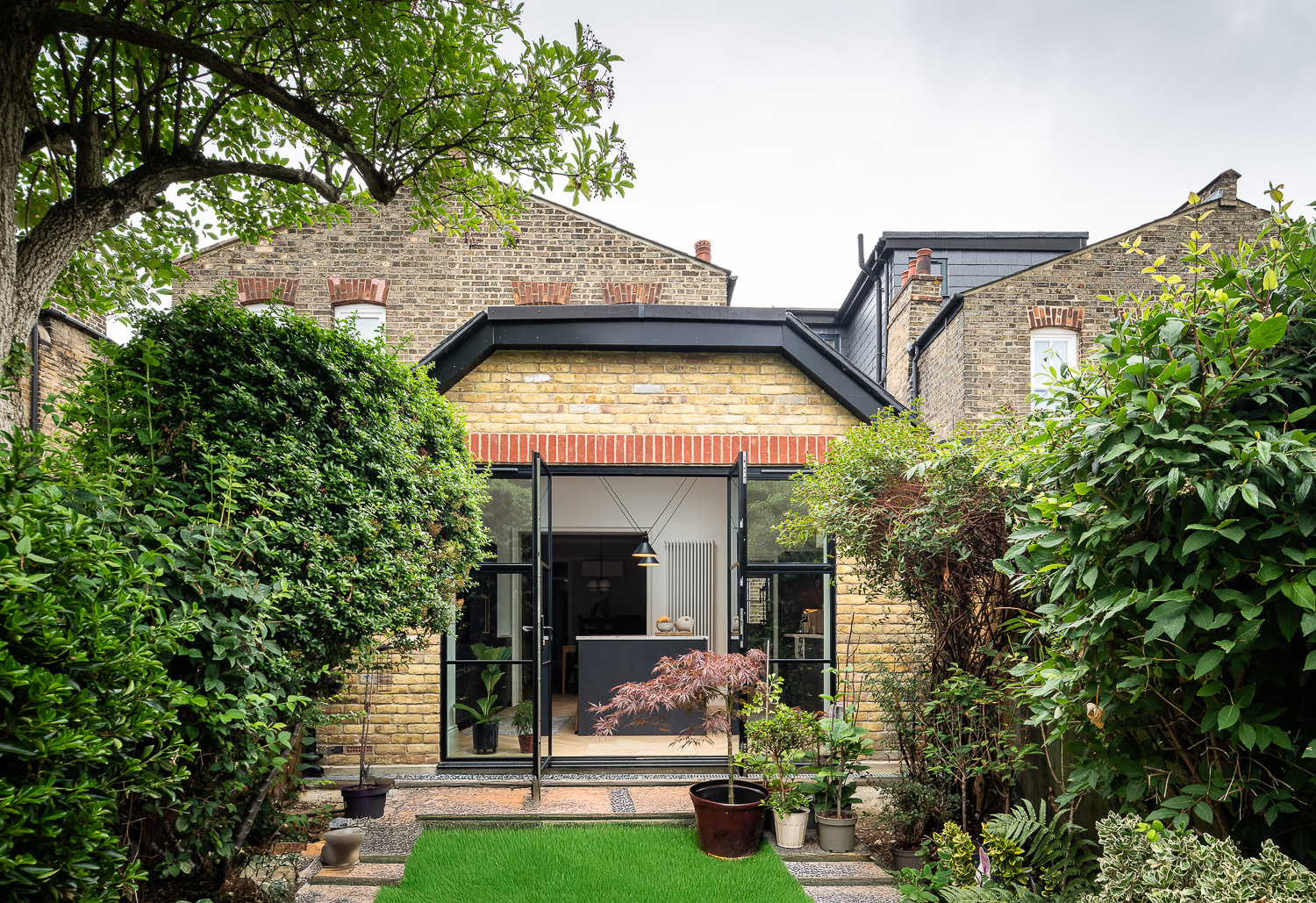 Rear extension of an Edwardian terrace with open steel-framed doors and landscaped garden.