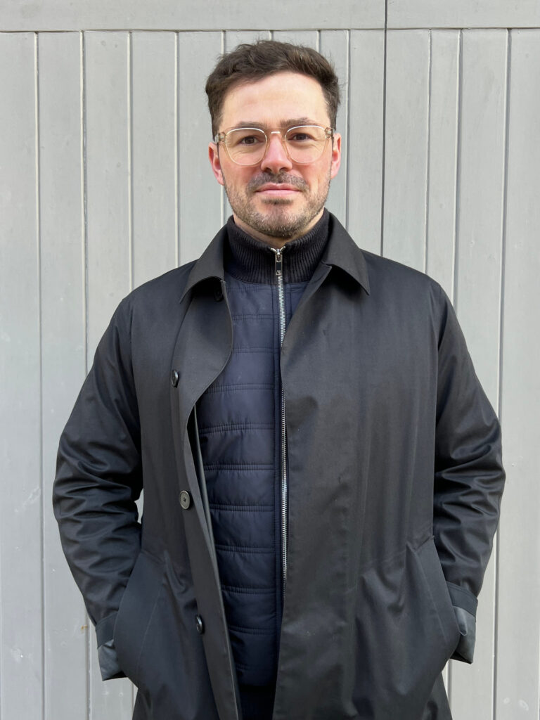 Portrait of the founder standing against a painted timber backdrop.