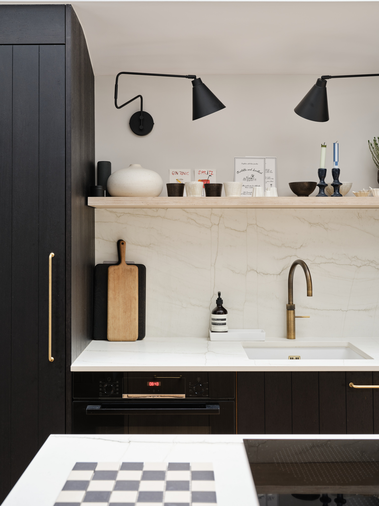 Black kitchen cabinetry with marble-effect splashback, brass tap, and sculptural wall lights