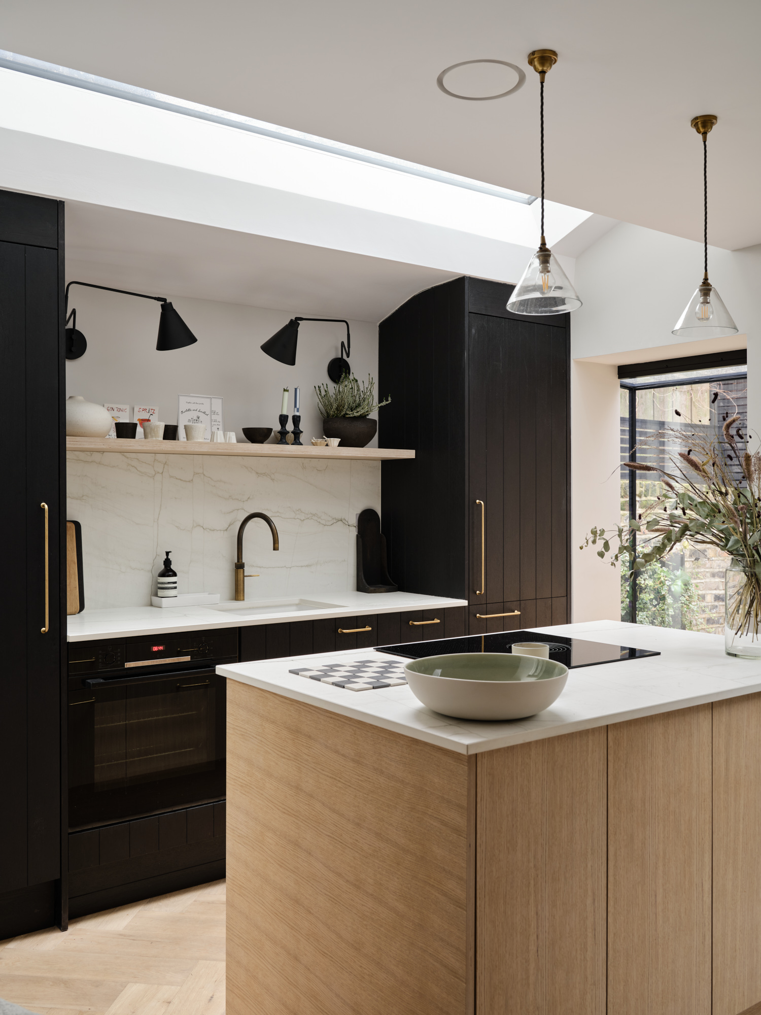 Kitchen island with oak joinery, black cabinetry, marble-effect splashback, and skylight