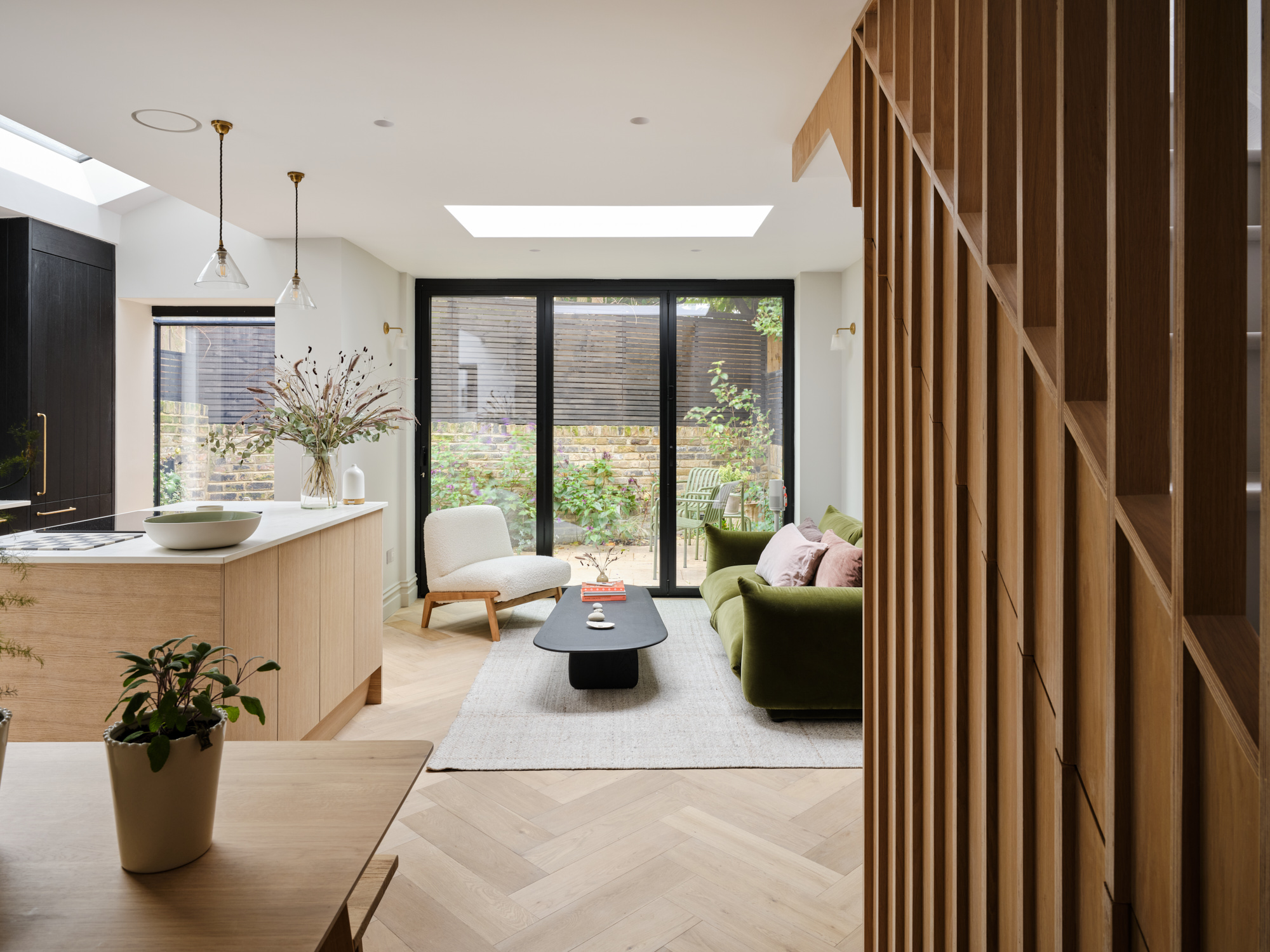 Open-plan living space with oak island, skylight, black cabinetry, and garden doors