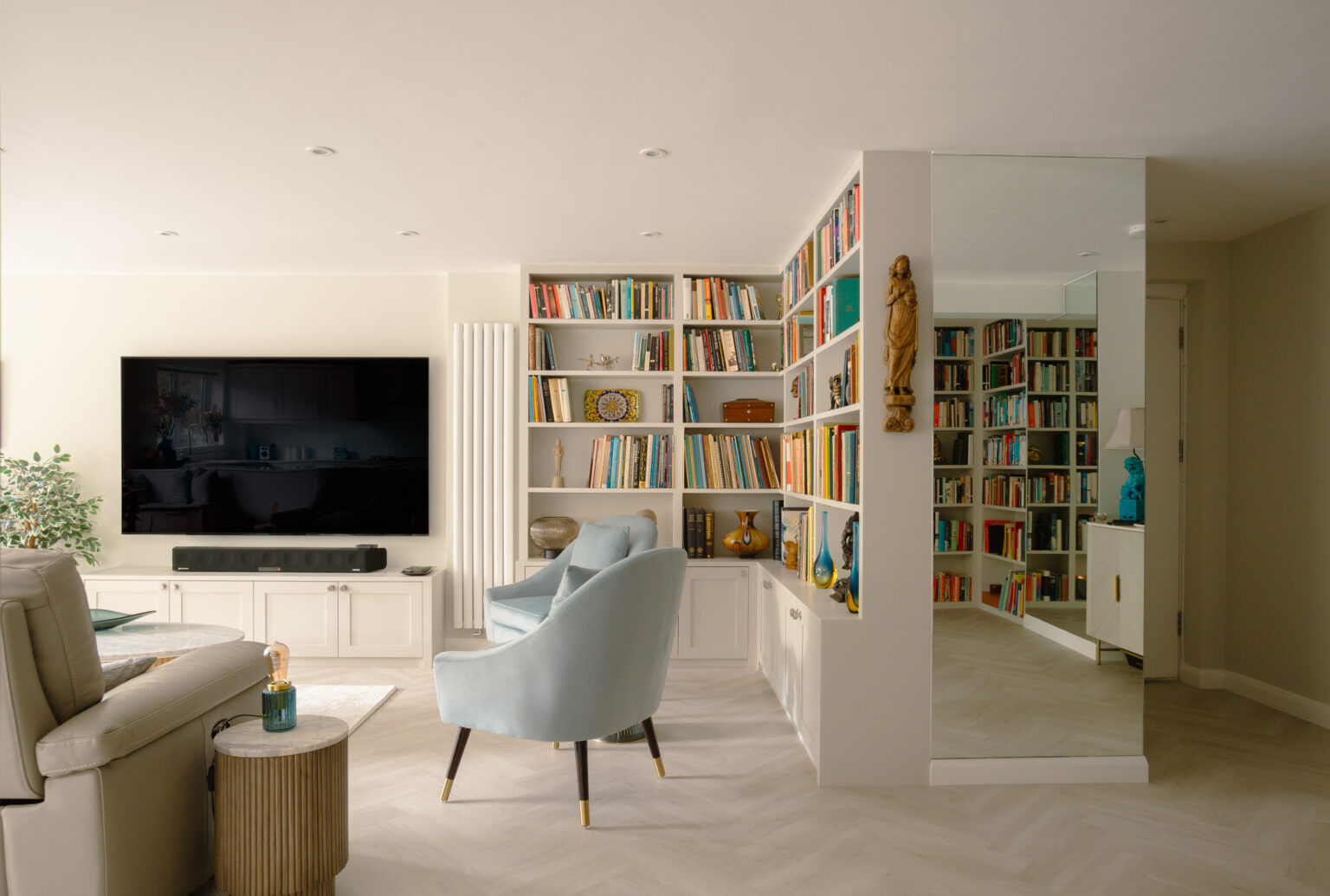 Open-plan living space with white bookshelves, television unit, pale blue armchair, and view through adjacent rooms