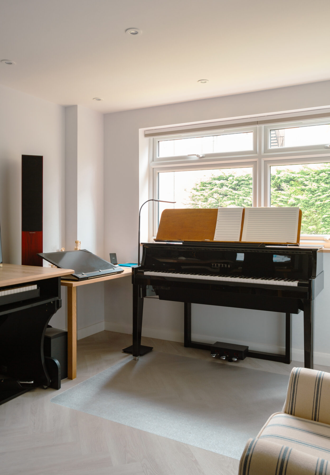 Study room with black grand piano positioned by large window with timber flooring and wooden desk