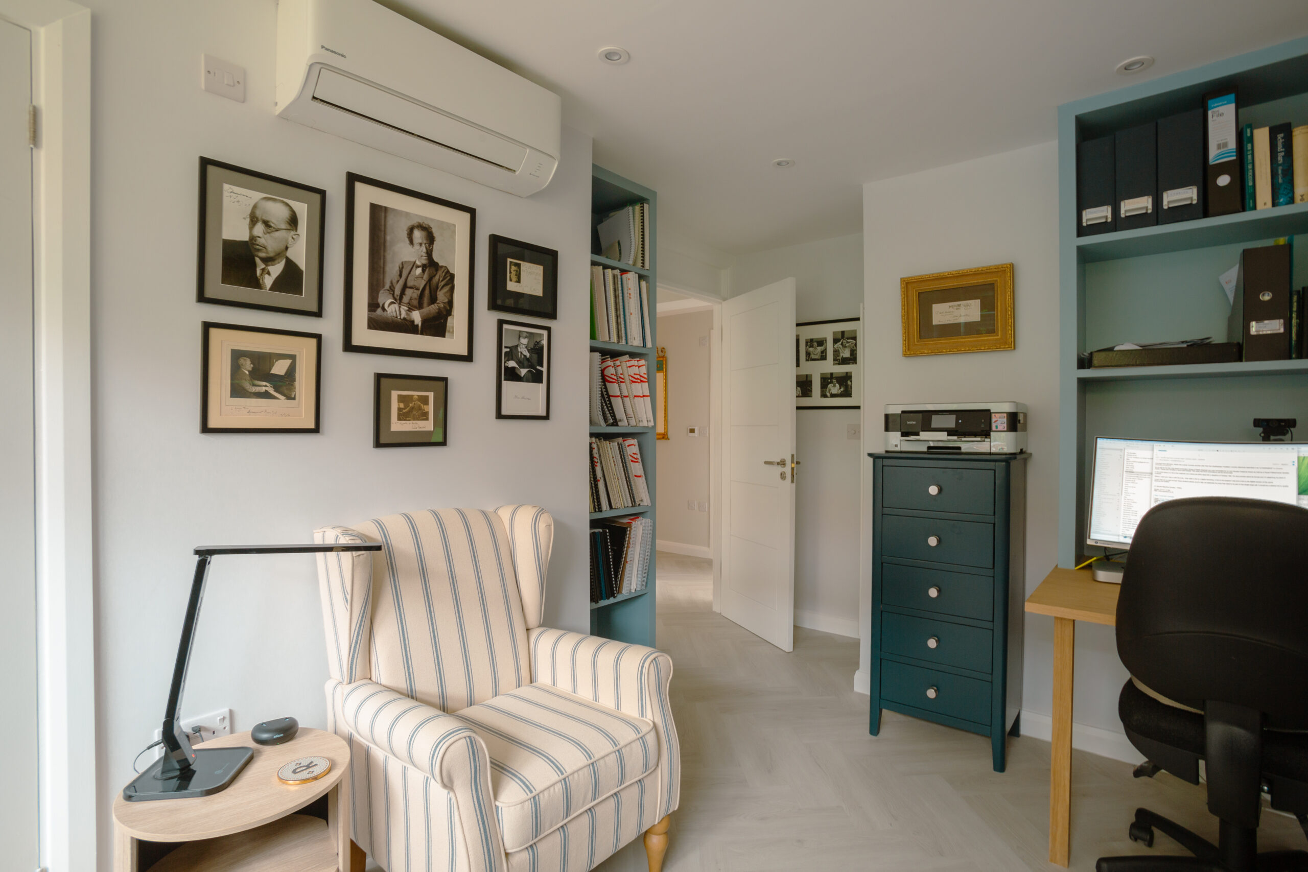 Home office with built-in teal shelving, striped armchair, and gallery wall of black-framed photographs